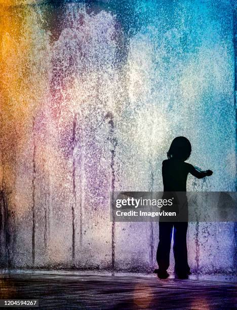 Silhouette of a child standing in a multi coloured water fountain, USA