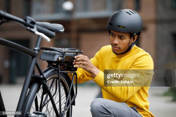 young man changing battery pack on electric bicycle - cycling helmet photos et images de collection