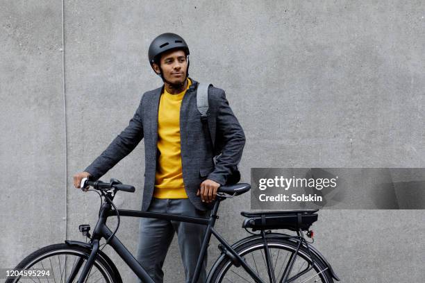 young man standing by electric bicycle - ciclista profesional fotografías e imágenes de stock