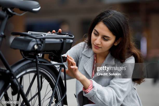 young woman changing battery pack on bicycle - elektrische fiets stockfoto's en -beelden