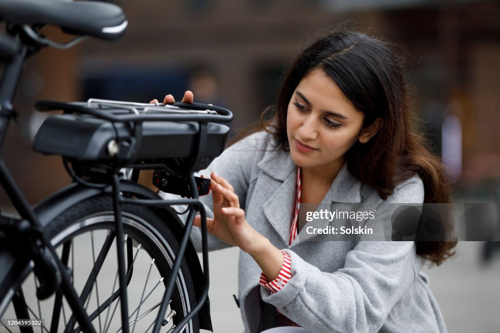 Young woman changing battery pack on bicycle