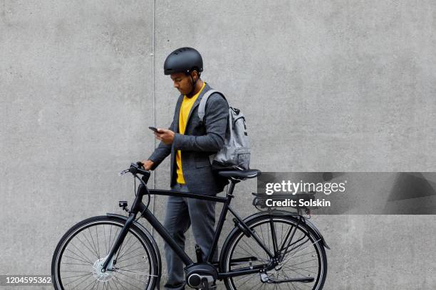 young man standing by electric bicycle using smartphone - commuter stockfoto's en -beelden