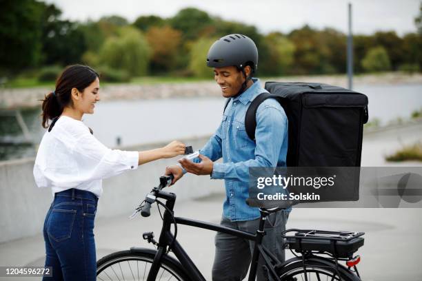 young man on electric bike with food delivery backpack getting contactless payment - pizza delivery stock pictures, royalty-free photos & images