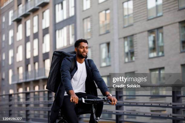 young man delivering take out food by electric bicycle - biking to work stock pictures, royalty-free photos & images