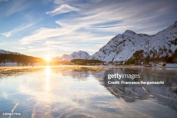 frozen surface of the alpine lake with signs of ice skates illuminated by sunset light. - moutain sunset snow stock-fotos und bilder