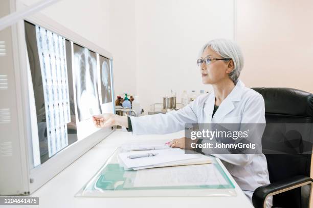 candid portrait of senior female doctor looking at x rays - doctor reaching stock pictures, royalty-free photos & images