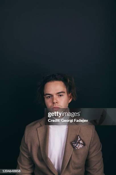 a dapper young man obviously you wearing a white turtleneck sweater and a beige jacket with handkerchief in his top breast pocket, looking pensively at his wrist watch, contemplating time - men costume black and white stock-fotos und bilder