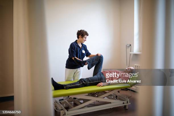 female physiotherapist helping senior man in pain - knees together - fotografias e filmes do acervo