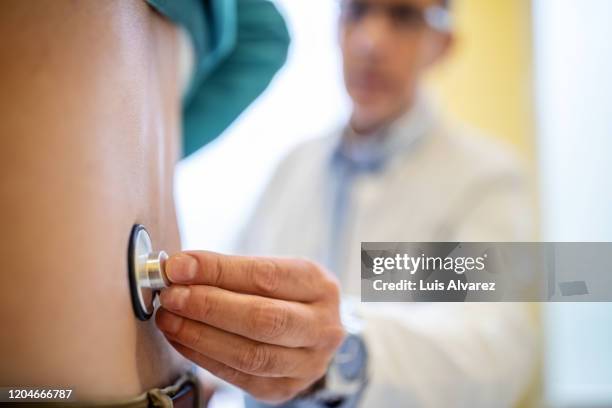 doctor examining patient with stethoscope - hausarzt stock-fotos und bilder