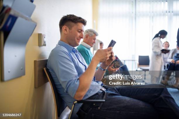 patients sitting in waiting room using mobile phone - man waiting foto e immagini stock