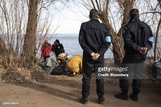 Frontex border officers stand by migrants from Afghanistan on the shore near the village of Skala Sikamineas on the island of Lesbos, Greece, on...