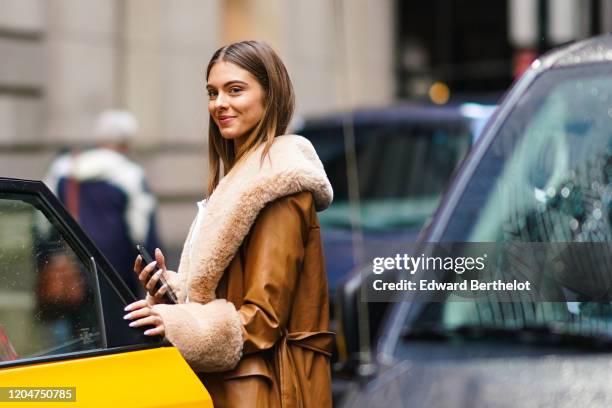 Guest wears a brown leather aviator jacket with fluffy wool inner lining, enters a taxi, outside Cinq a Sept, during New York Fashion Week Women's...