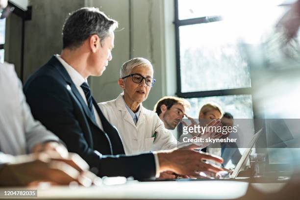 senior doctor and businessman using computer on a meeting with their colleagues. - medical conference stock pictures, royalty-free photos & images