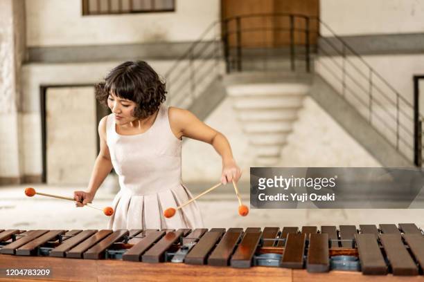 asian young woman plays marimba in a ruin with large windows. - xylophone stock-fotos und bilder