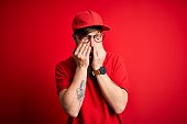 Young handsome delivery man wearing glasses and red cap over isolated background rubbing eyes for fatigue and headache, sleepy and tired expression. Vision problem