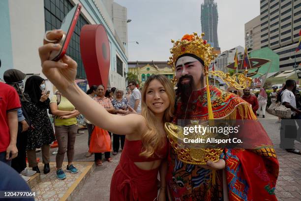 An ethnic Chinses girl poses for selfie with a man dressed like " Chinese God of Fortune " during the Lantern Festival celebration or in hokkien "...