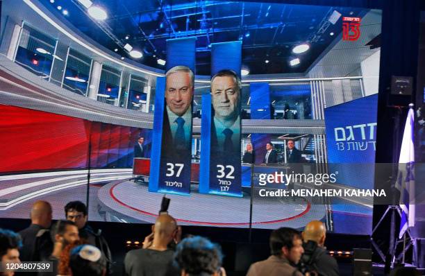 This picture taken on March 2, 2020 shows people standing before a giant screen displaying a broadcast from Israel's Channel 13 with an exit poll...