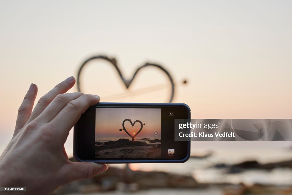Woman photographing heart shape through phone