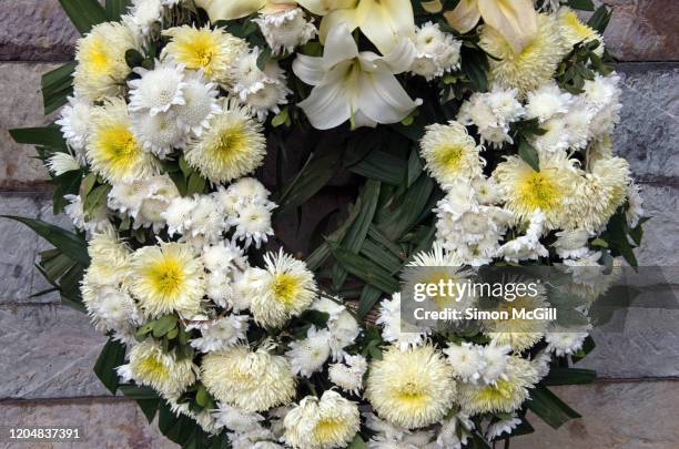 wreath of white flowers against a stone wall - monumento conmemorativo fotografías e imágenes de stock