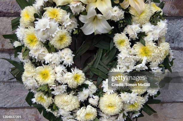 wreath of white flowers against a stone wall - funeral flowers stockfoto's en -beelden