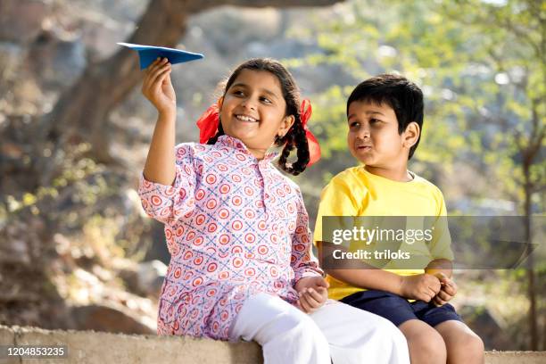 junge und mädchen spielen mit papier flugzeug - indian kid inspiration stock-fotos und bilder