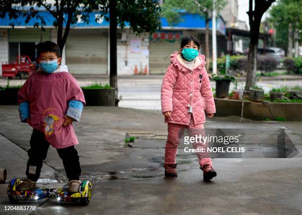 Children wearing face masks walk along a street in Yueyang, Hunan province on March 3, 2020. - The world has entered uncharted territory in its...