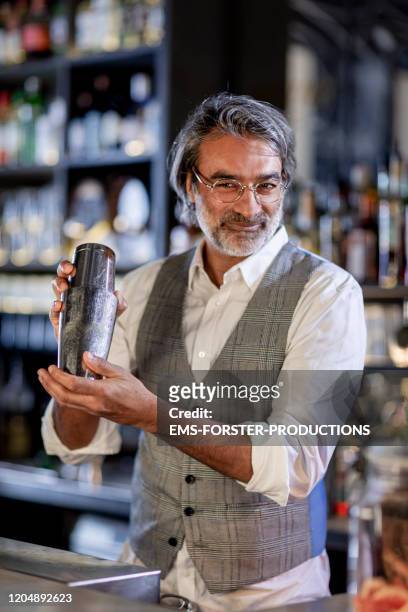handsome bartender shaking cocktail with shaker in cocktail bar at night - craft cocktail stock pictures, royalty-free photos & images