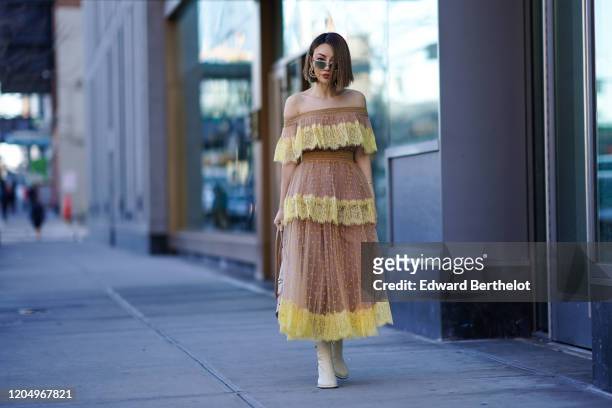 Jessica Wang wears an off-shoulder pleated and ruffled mesh lace dress with yellow parts, earrings, sunglasses, white boots, outside Self Portrait,...