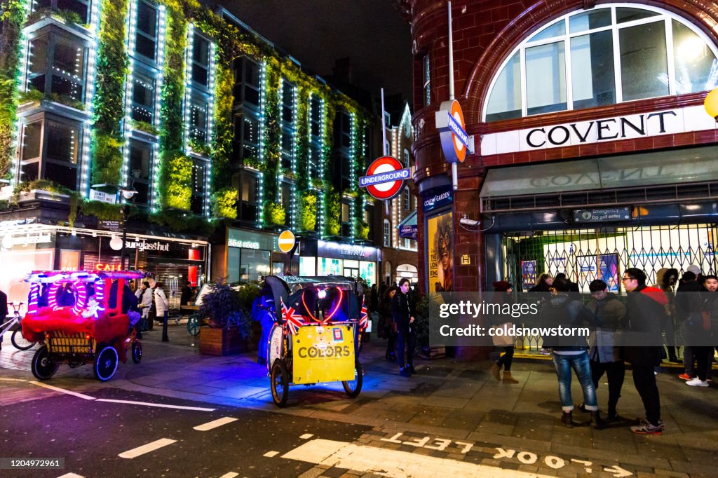 Rickshaws and crowd of people outside Covent Garden tube station at night in central London
