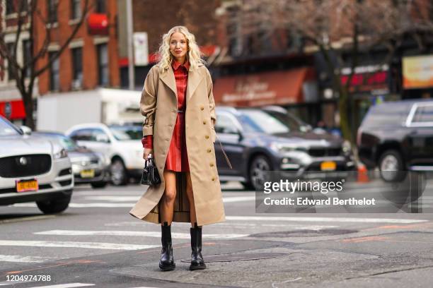 Leonie Hanne wears a light brown trench coat a red leather dress, black leather boots, a bag, outside Longchamp, during New York Fashion Week...