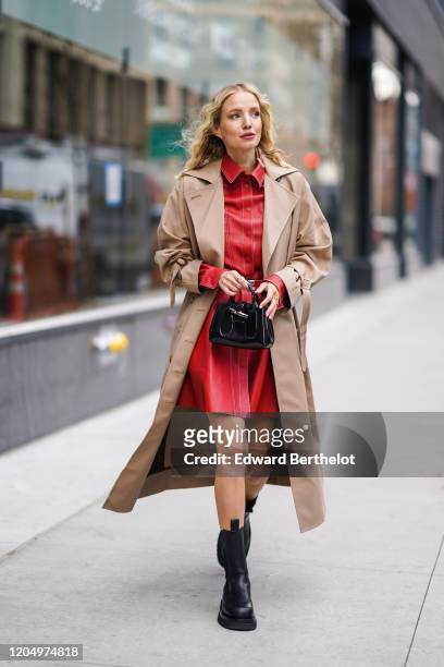 Leonie Hanne wears a light brown trench coat, a red leather dress, black leather boots, a bag, outside Longchamp, during New York Fashion Week...