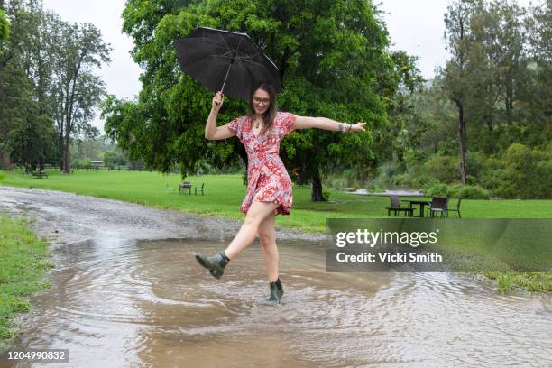 young female in a red dress and boots with a black umbrella dancing in a puddle - queensland storm stock pictures, royalty-free photos & images