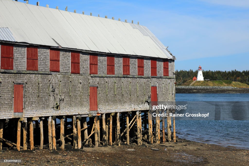 Old wooden house on piles on the bay shore with an old lighthouse on the opposite side of the bay