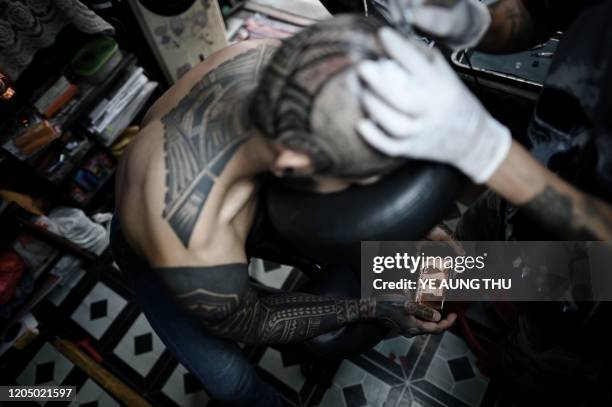 This photo taken on February 26, 2020 shows gym trainer Myo Thet Paing watching the "Lion King" movie during an inking session at a tattoo shop at...
