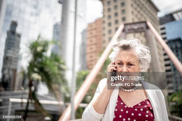 rabbia anziana imprenditrice che cammina e parla al cellulare in città - complaining foto e immagini stock