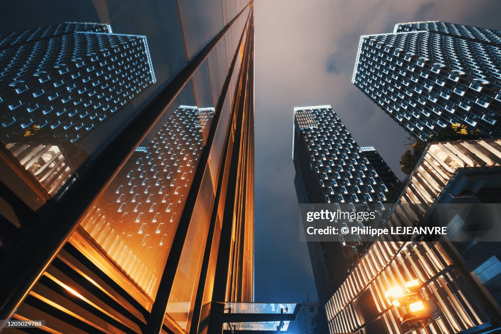 Modern skyscrapers illuminated at night reflecting on a glass facade low angle view