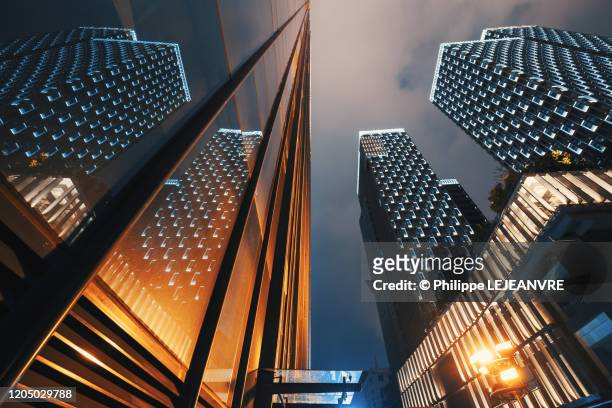 modern skyscrapers illuminated at night reflecting on a glass facade low angle view - torre struttura edile foto e immagini stock