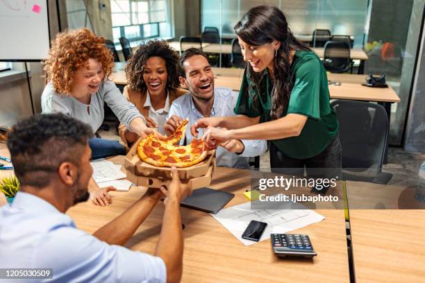 gemeinsames mittagessen. glückliches multikulturelles team, das pizza isst und miteinander kommuniziert, während man im modernen büro sitzt - coworkers having fun stock-fotos und bilder