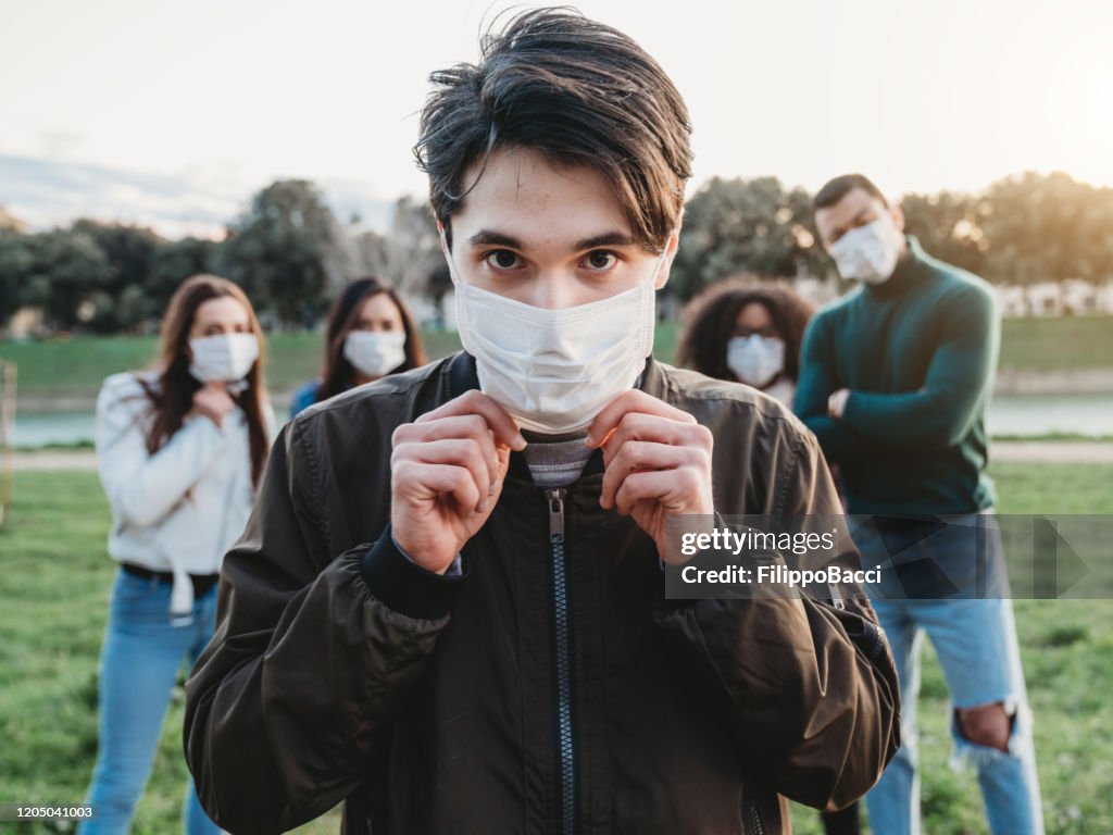 Young adult man wearing a pollution mask to protect himself from viruses. His friends are in the background.