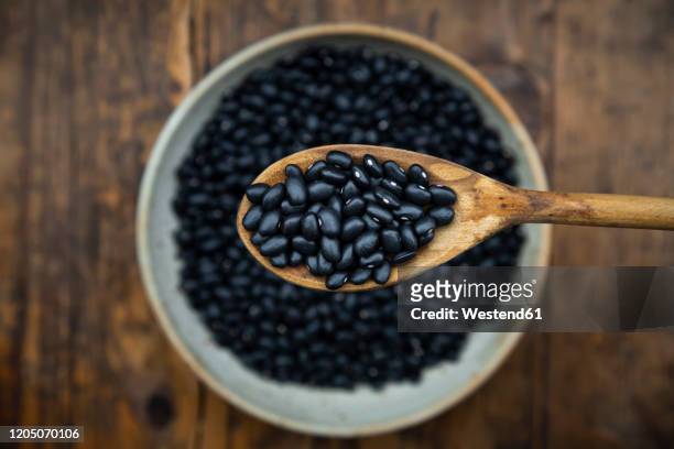 overhead view of spoon and bowl of black bean on wooden table - bean stock pictures, royalty-free photos & images