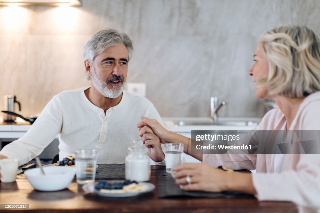 Affectionate mature couple sitting at table in kitchen at home having breakfast