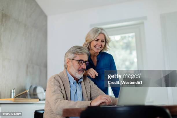mature man with wife using laptop on kitchen table at home - daily life in belgium stock pictures, royalty-free photos & images