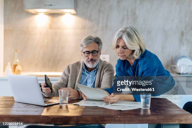 mature couple with papers and laptop on kitchen table at home - mature couple stock pictures, royalty-free photos & images