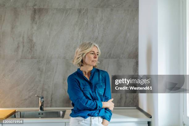 portrait of pensive mature woman in kitchen at home - pensive bildbanksfoton och bilder