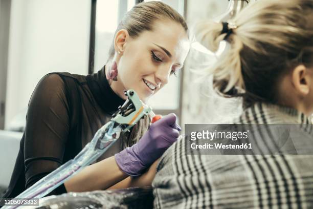 female tattooist tattooing upper arm of female customer - tattooing 個照片及圖片檔