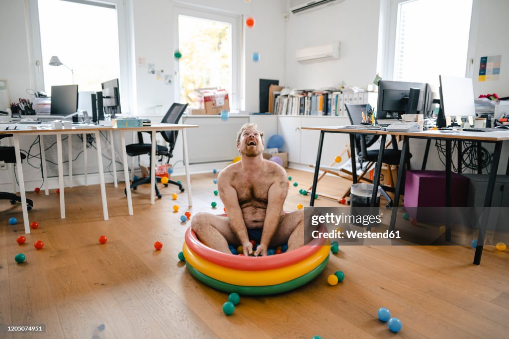 Crazy businessman sitting in wading pool in office playing with balls