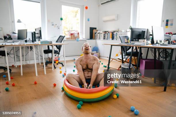 crazy businessman sitting in wading pool in office playing with balls - erwachsene person stock-fotos und bilder