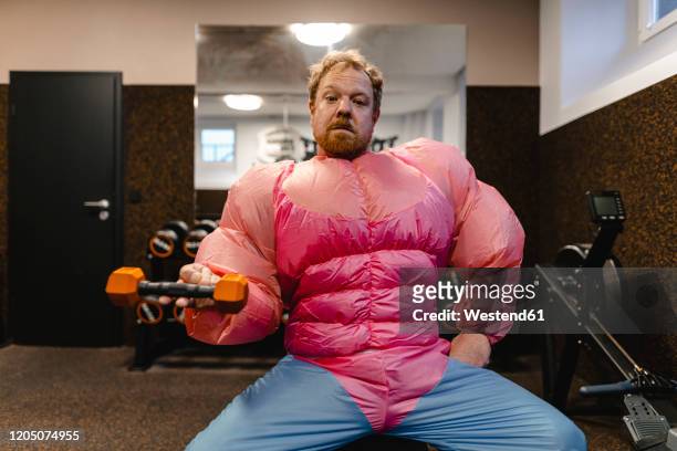 man in gym wearing pink bodybuilder costume lifting dumbbell - männlichkeit stock-fotos und bilder