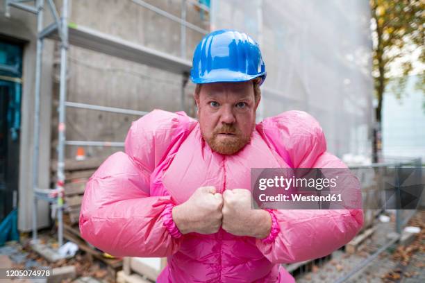 portrait of man wearing pink bodybuilder costume and hard hat at construction site - strong foundations stock pictures, royalty-free photos & images