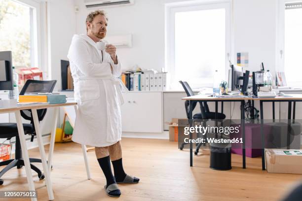 businessman wearing bathrobe in office holding cup - bademantel stock-fotos und bilder